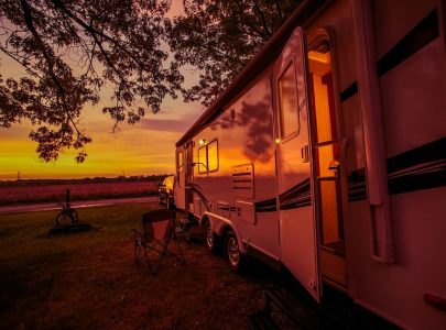 RV Camping Spot at Scenic Sunset. Camper Traveling. Pulling Travel Trailer by Car.
